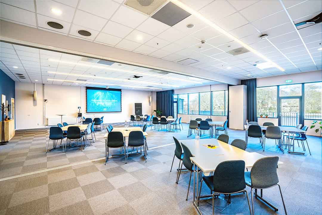 Subbe Fyr möblerad för konferens med flera bordsgrupper, projektorduk och fönstervägg mot Nöjesparken